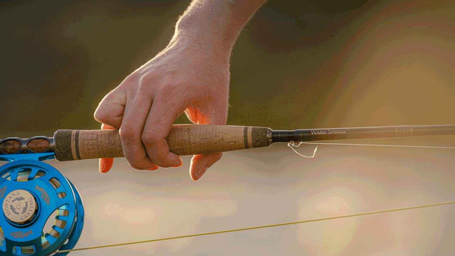 Hand holding a fly fishing rod with a blurred background