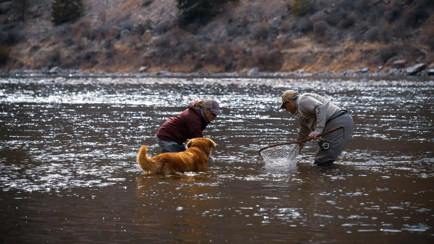 Fly Fisherman Holding Fly Fishing Rod Releases Trout While Woman and Dog Watch